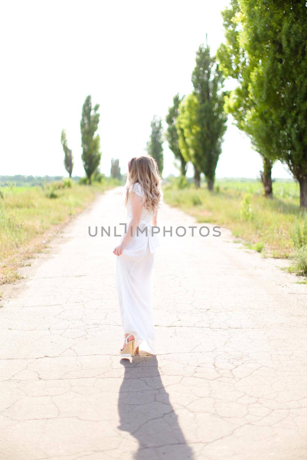 Back view of young european woman wearing white dress walking on road. by sisterspro