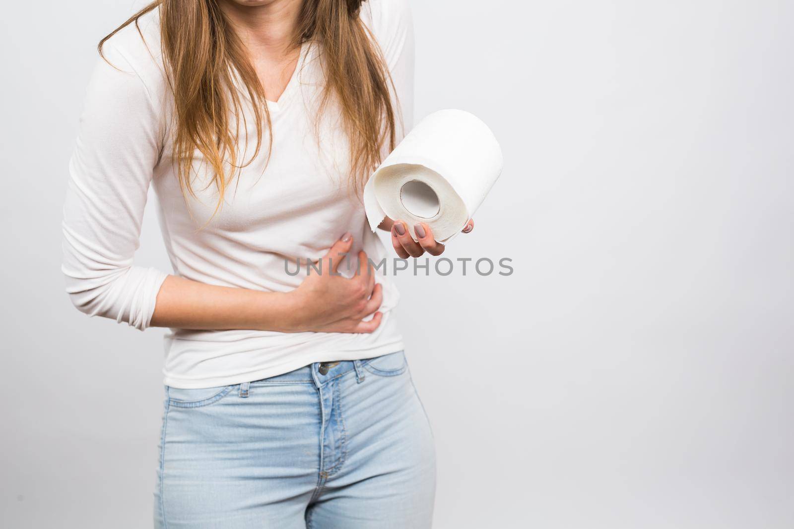 Woman with stomach pain and toilet paper roll on white background.