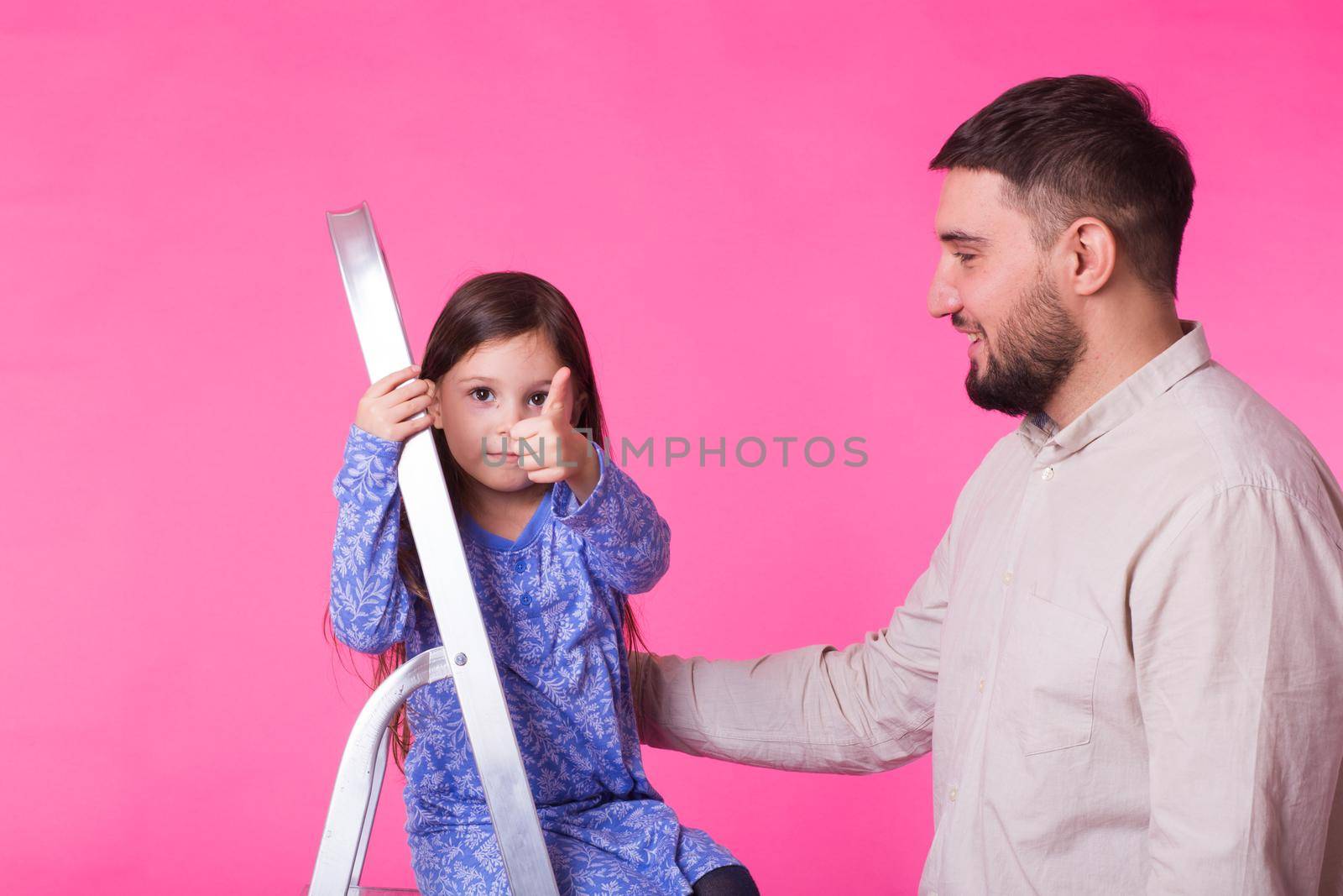 Father and her little daughter over pink background. Adult man and baby girl are happy.