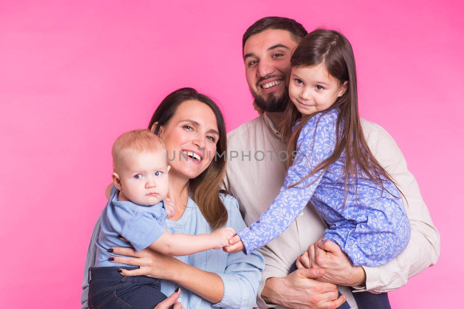 Cute family posing and smiling at camera together on pink background.