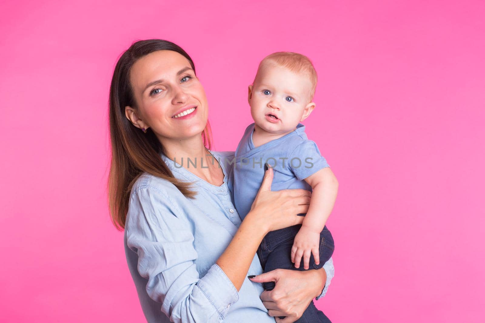 Loving mother playing with her baby boy on pink background.