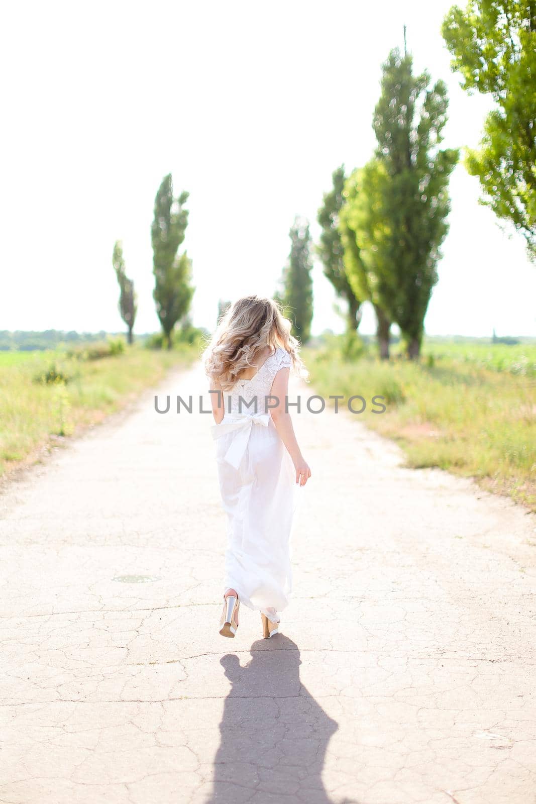 Back view of european woman wearing white dress walking on road. by sisterspro