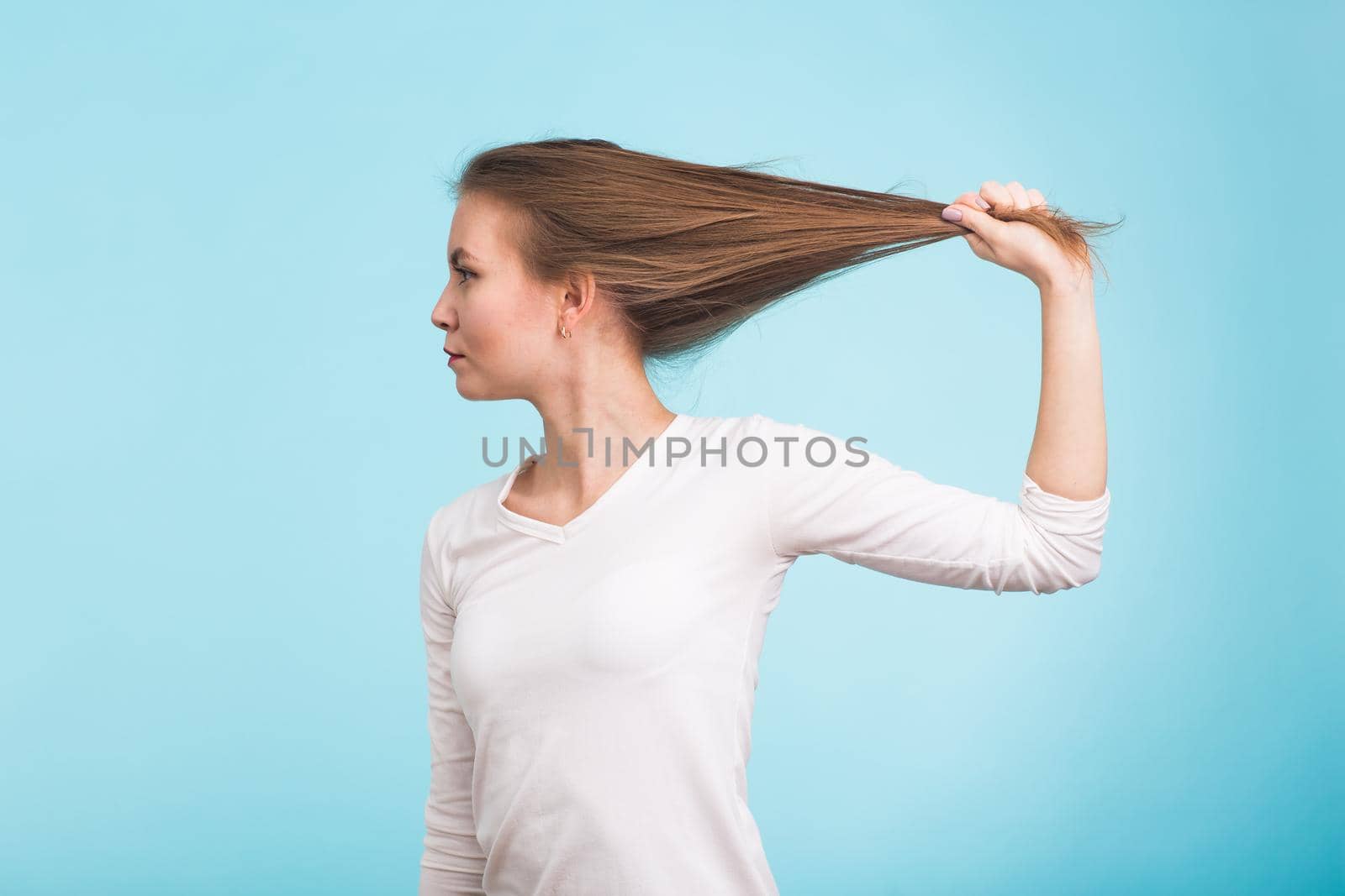 Attractive woman holding to the hair. Healthy and strong hair on blue background