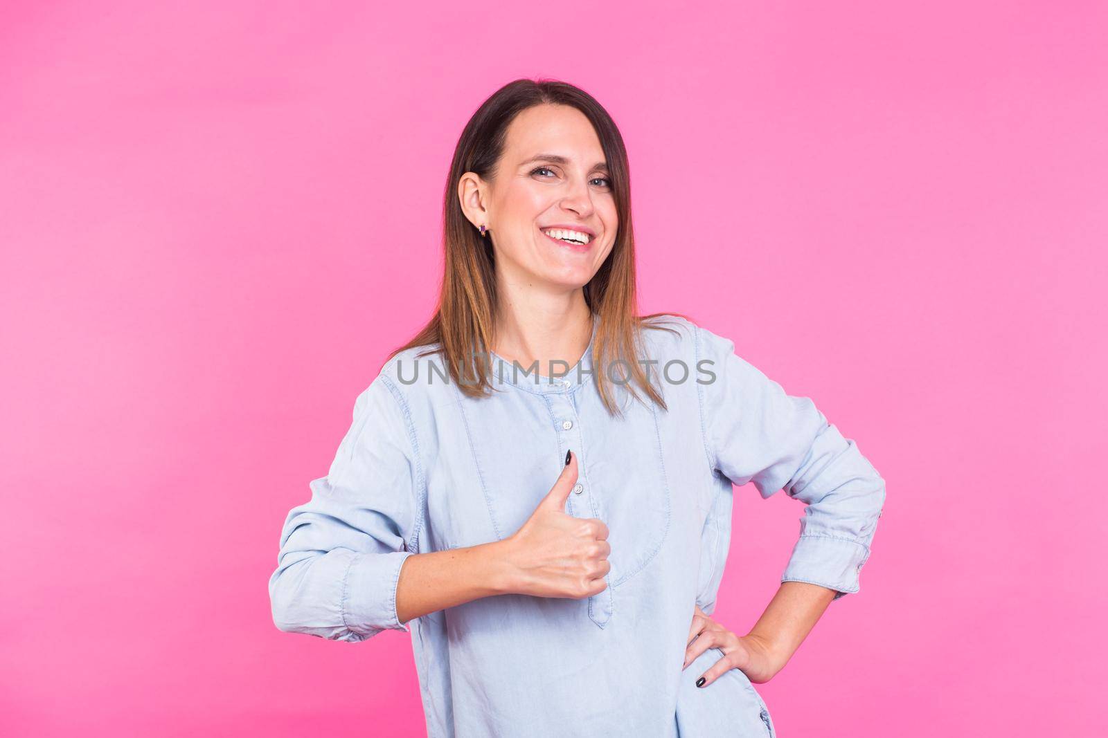 Smiling Woman in shirt posing in studio and showing thumbs up on pink background by Satura86