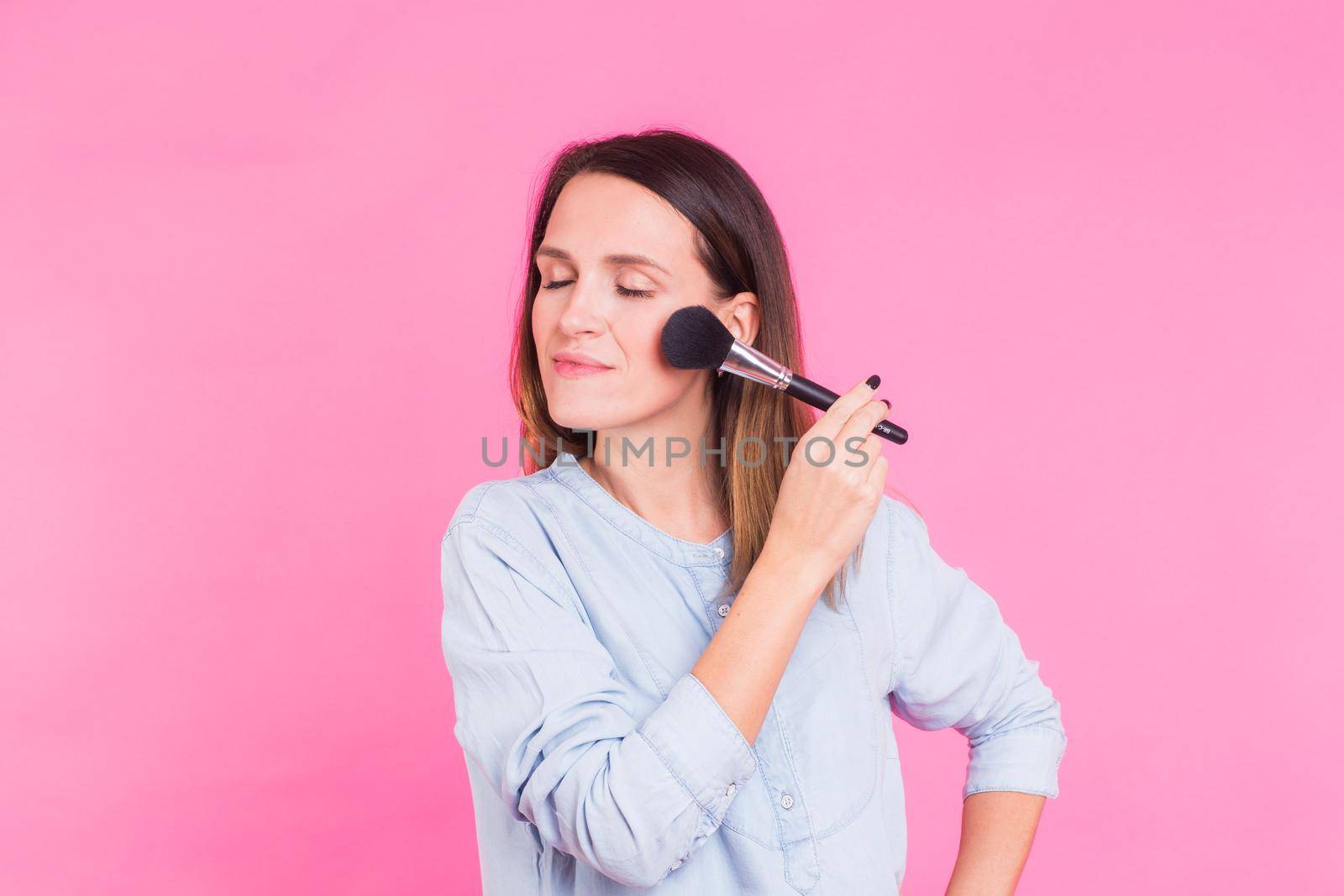 Portrait of makeup artist with brushes in hand on a pink background