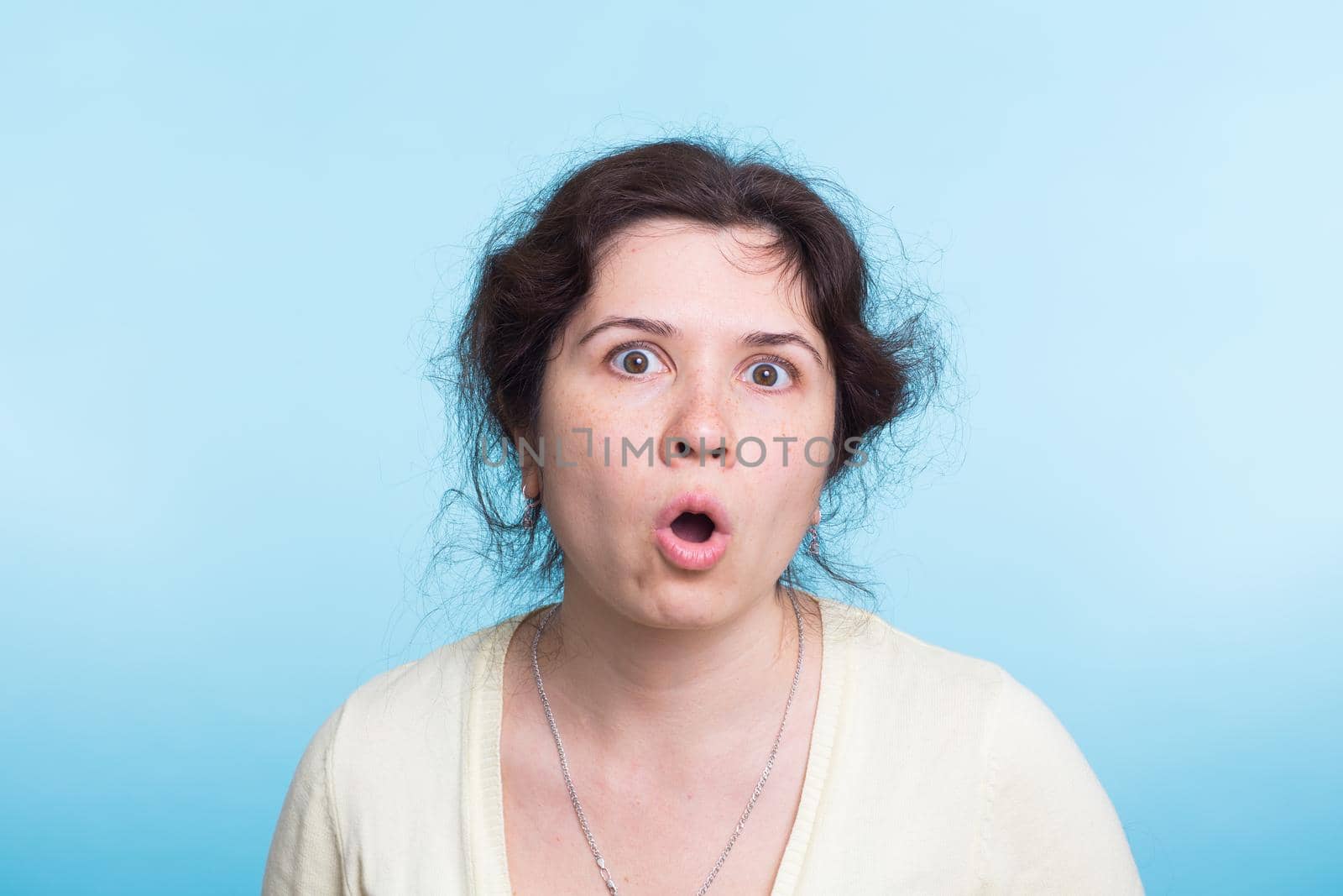 shocked young woman, isolated against blue studio background.