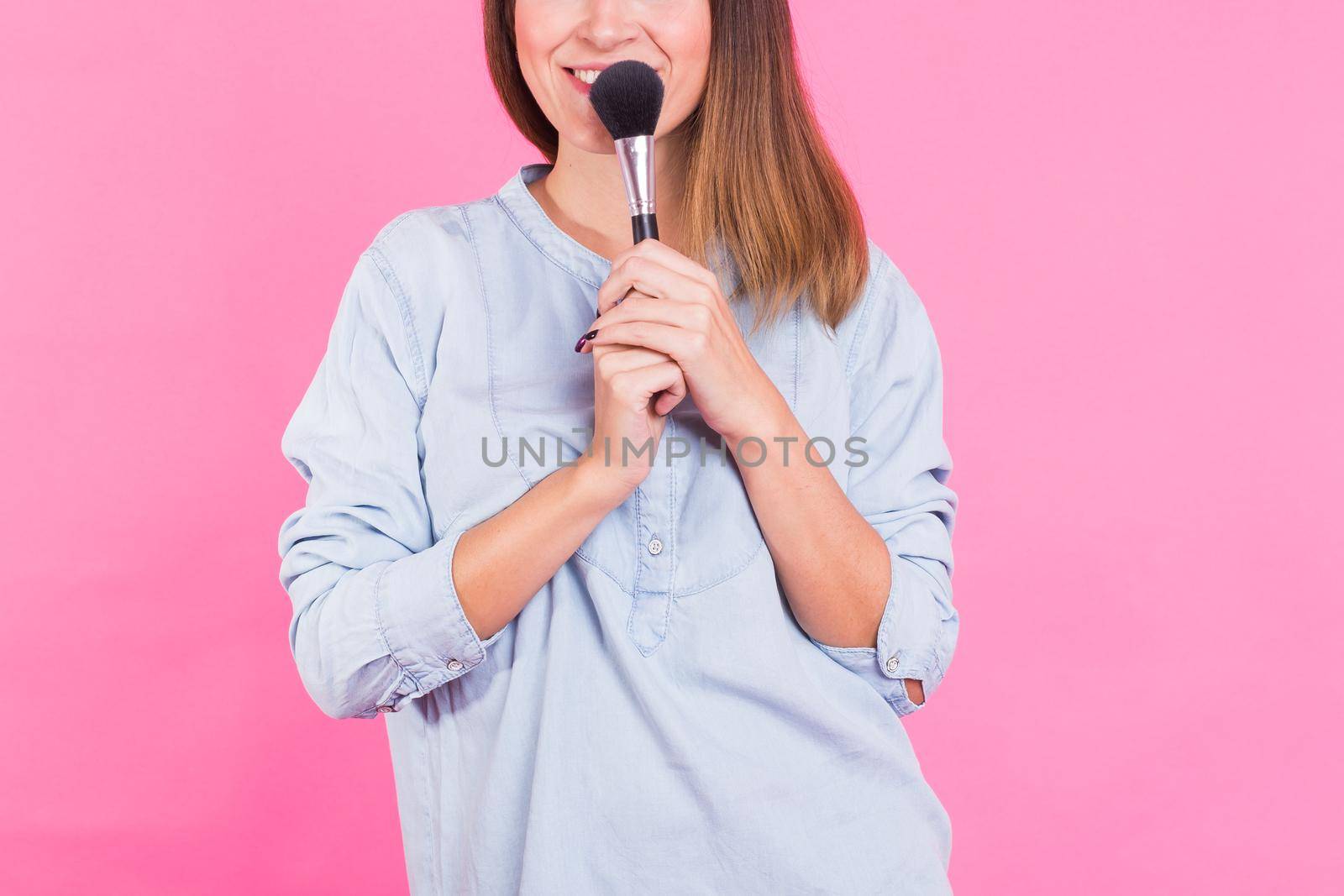 Professional makeup artist with brushes on pink background.