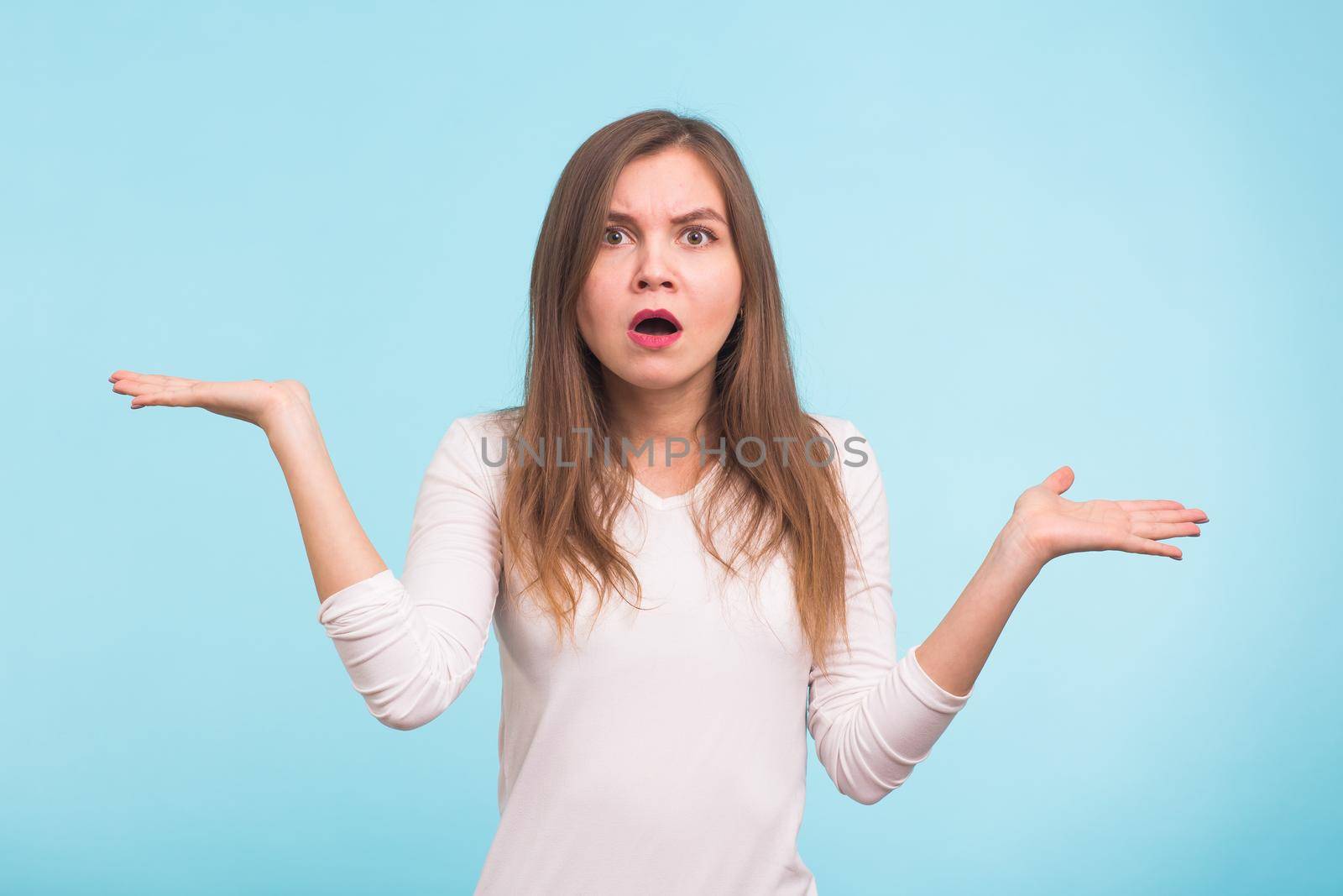 Portrait of a young woman shrugging shoulders over blue background.