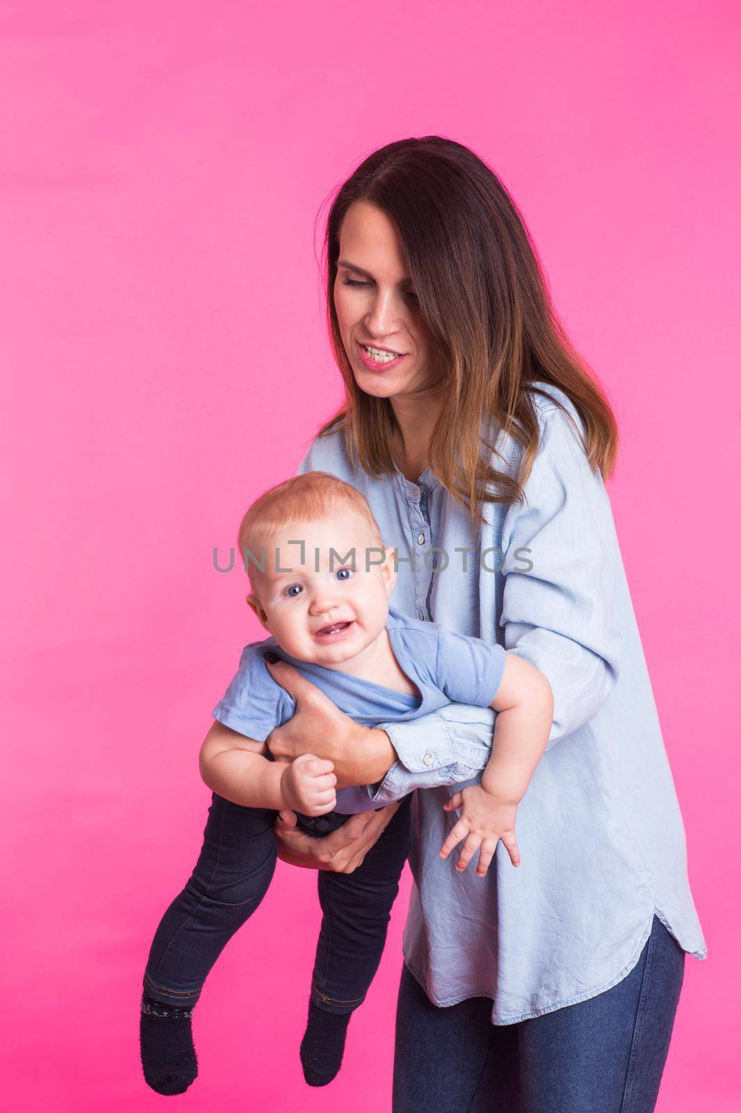 family, motherhood, parenting, people and child care concept - happy mother holds adorable baby over pink background.