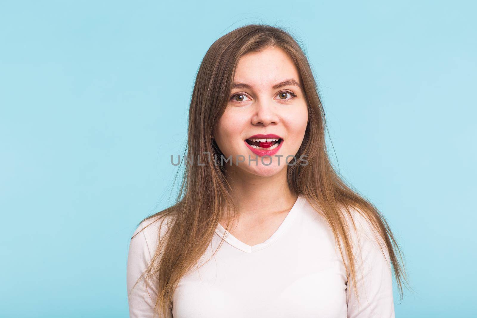 Red tablet in the mouth of the woman on blue background.