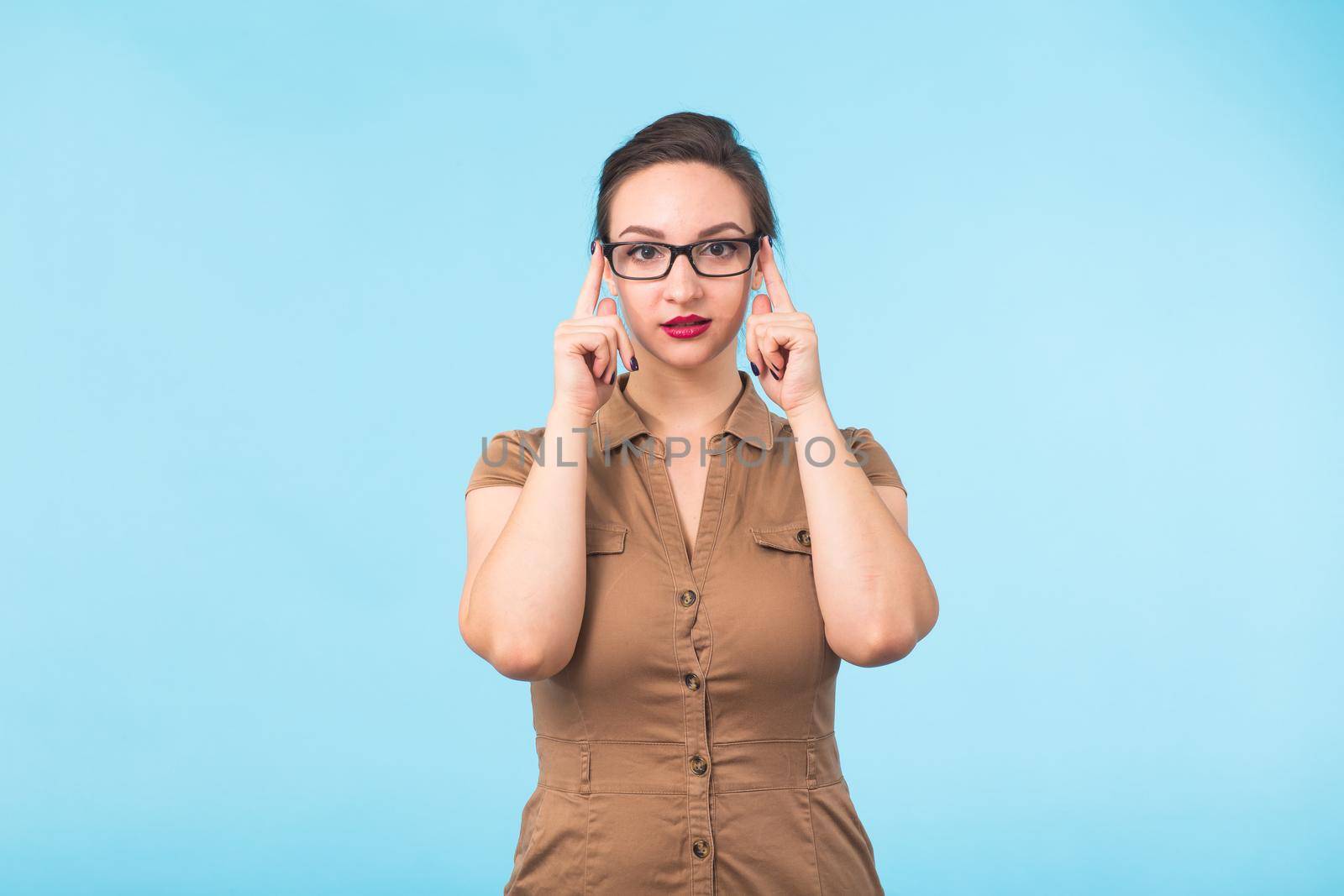 Elegant cheerful brunette in eyeglasses smiling at camera on blue background with copy space by Satura86