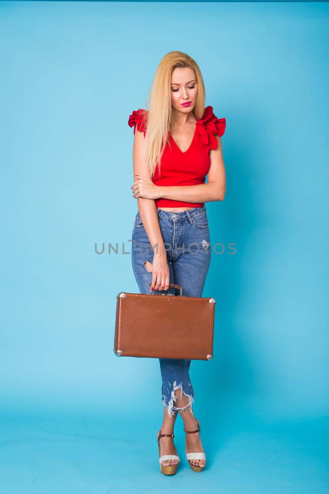 Summer, fashion and holiday concept - Beautiful blonde woman with retro suitcase on blue background.