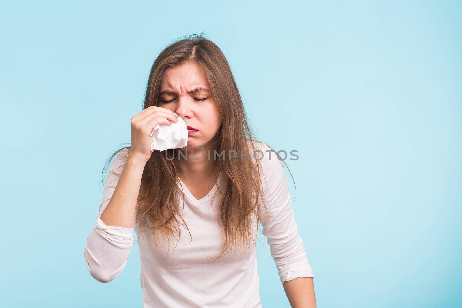 Young woman has a runny nose on blue background.