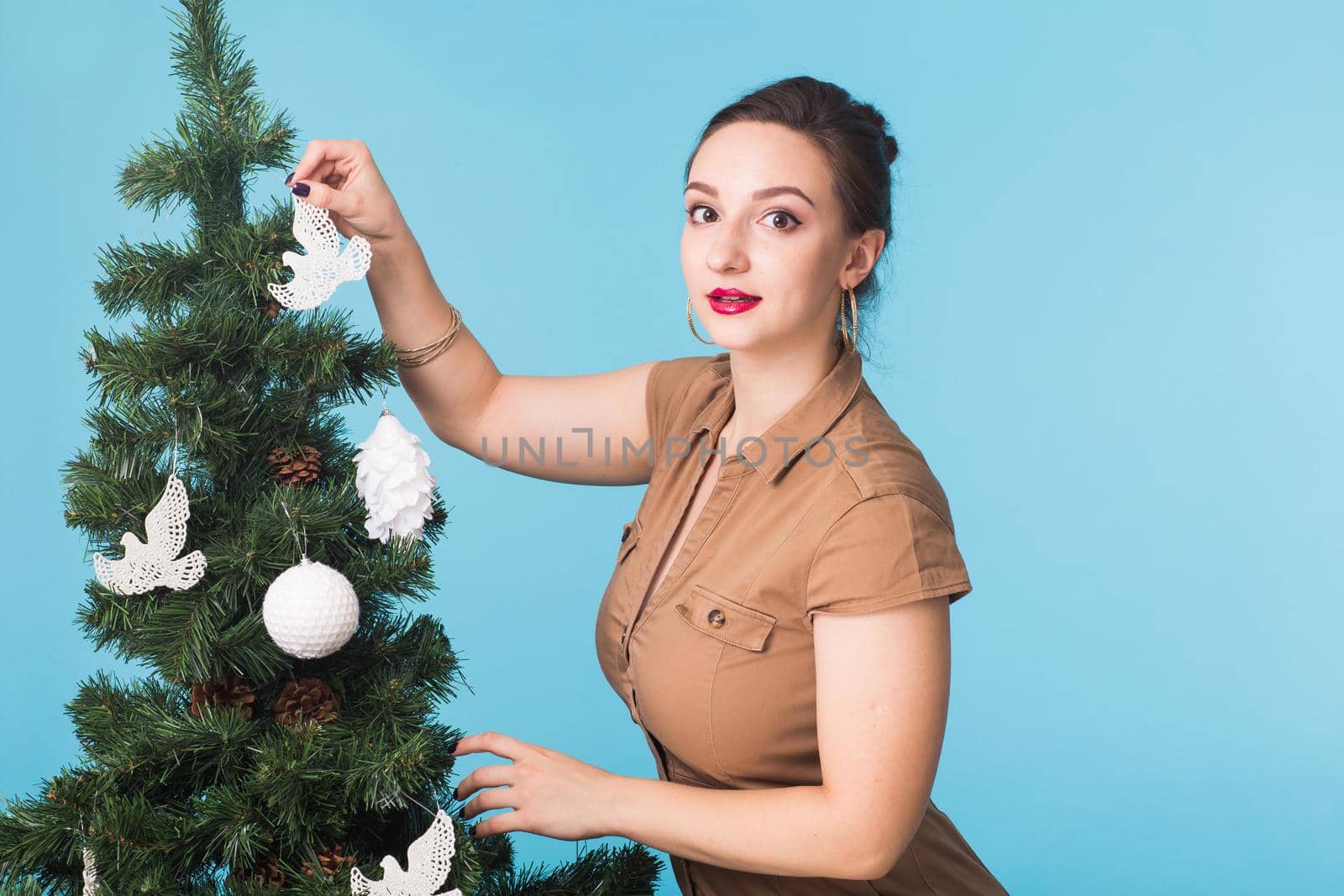 People and holidays concept - Portrait of smiling young woman with Christmas tree on blue background
