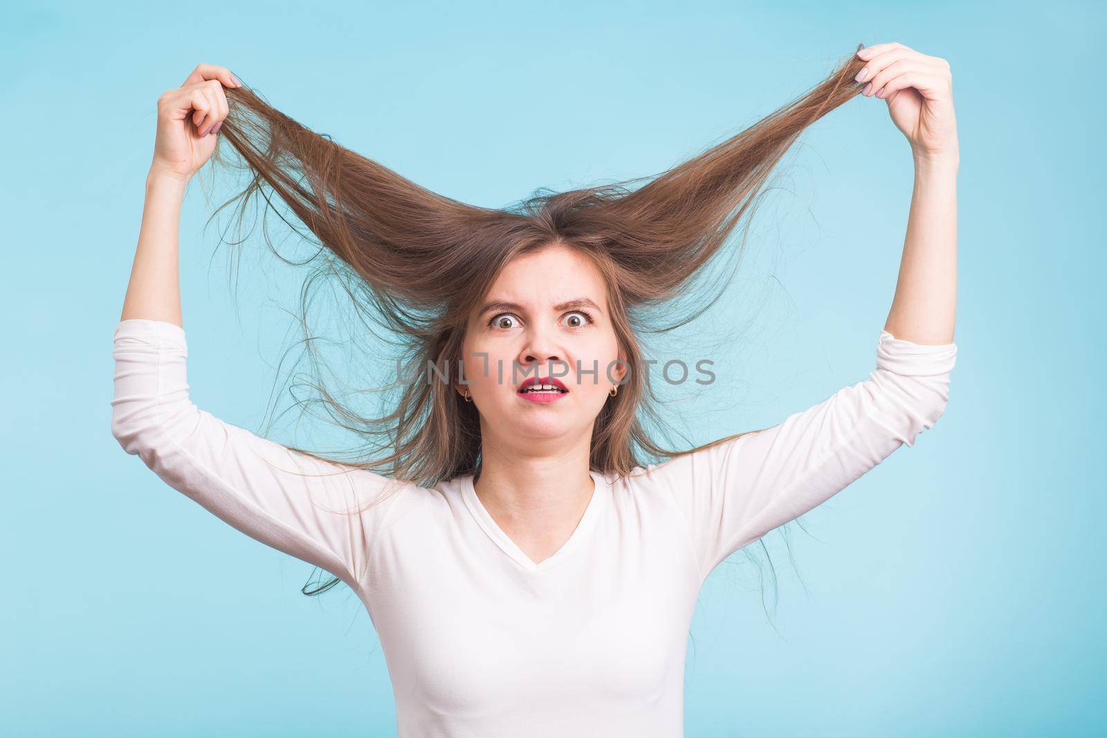 Young woman with unhealthy long hair keep hair in hand with nature make up portrait isolated on blue by Satura86