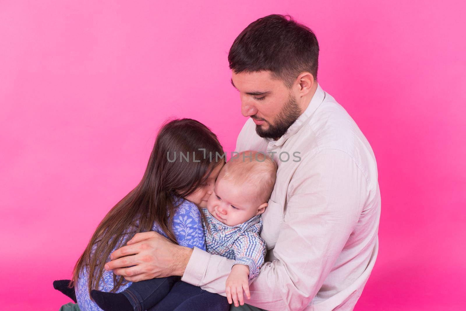 handsome father carrying his little daughter and baby son on pink background.
