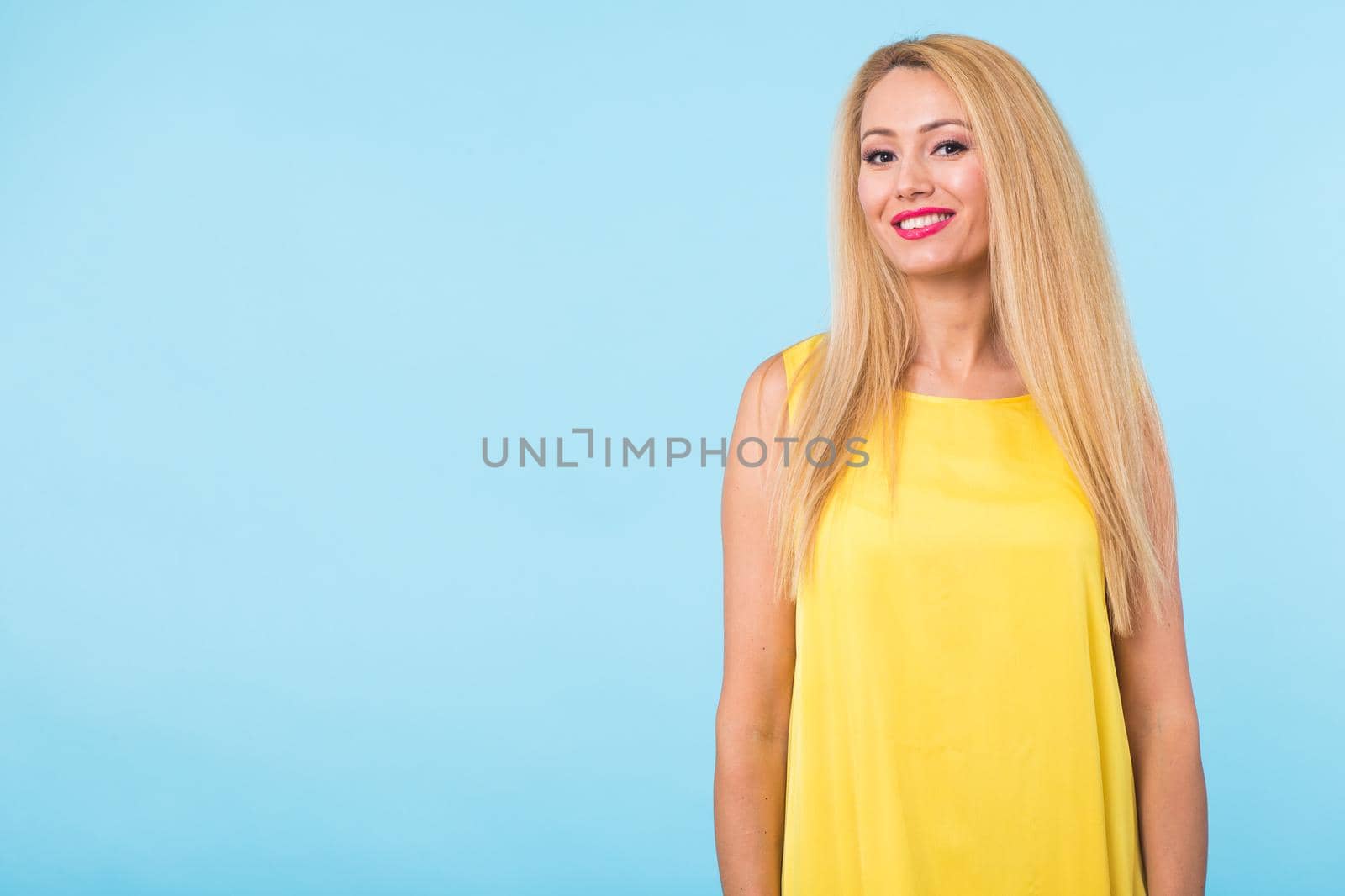 beauty fashion summer portrait of blonde woman with red lips and yellow dress on blue background with copy space.