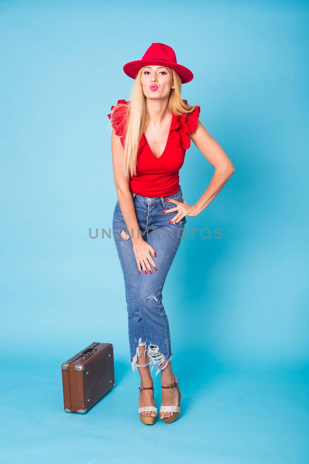 Summer, travel, people and holidays concept - fashionable young blond woman with retro suitcase isolated on blue background.