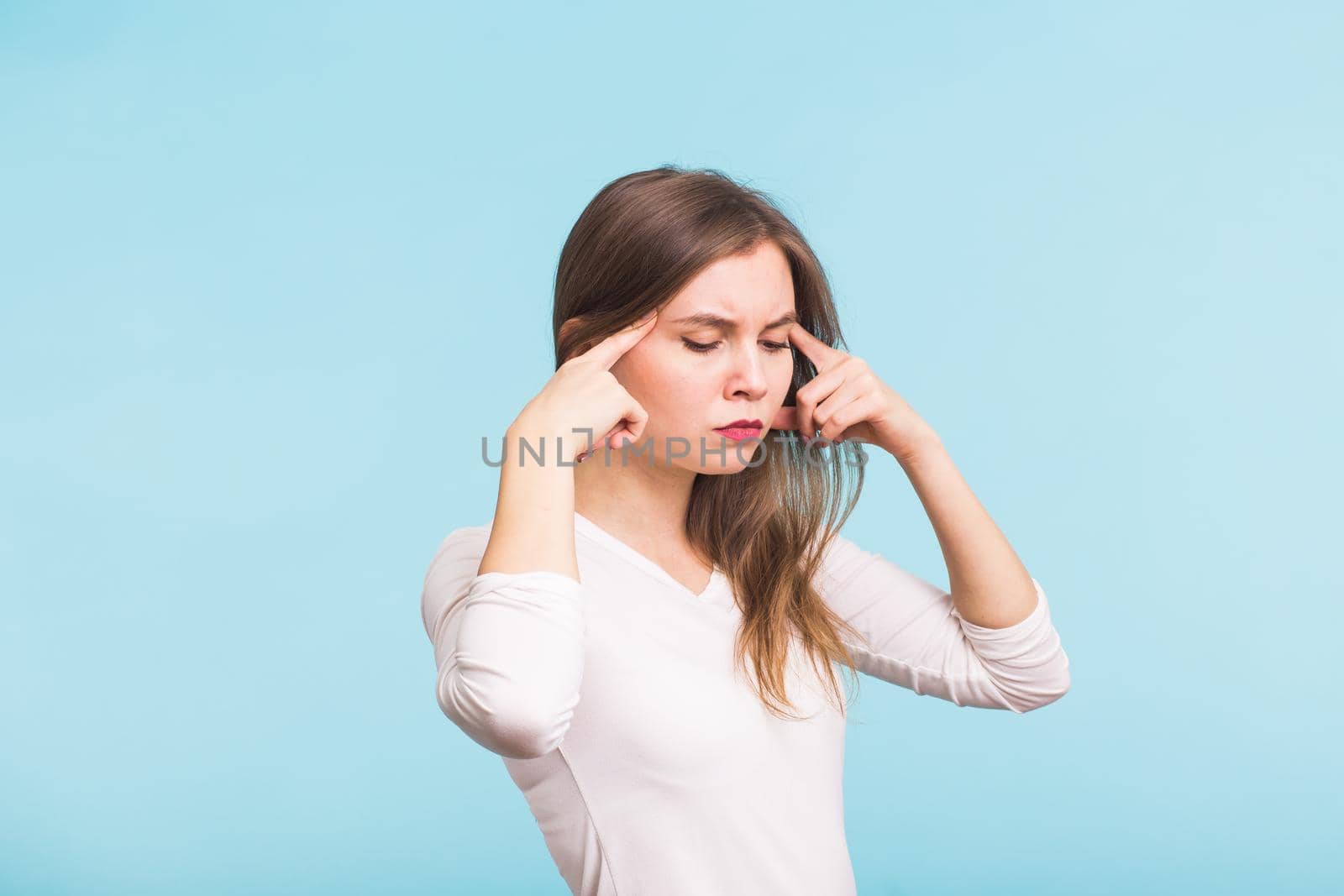 Portrait of beautiful young woman with bare shoulders touching her temples feeling stress, on blue background.