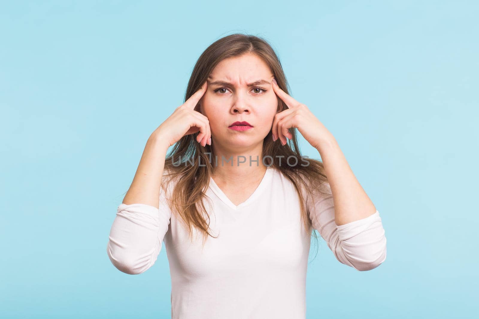 Portrait of beautiful young woman with bare shoulders touching her temples feeling stress, on blue background.