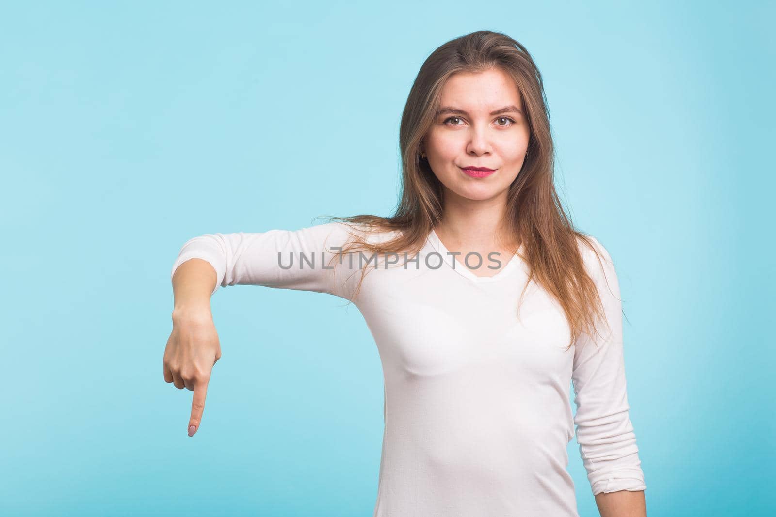 Young woman pointing at copy space on blue background.