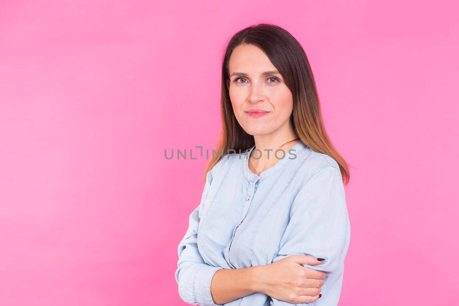 Portrait of a beautiful woman with long brown hair wearing blue cotton blouse, standing waist up smiling on a pink background by Satura86