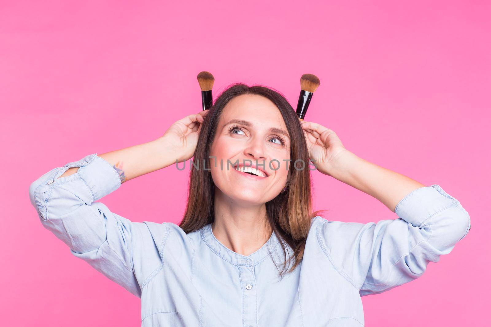 Funny makeup artist with brushes on pink background.