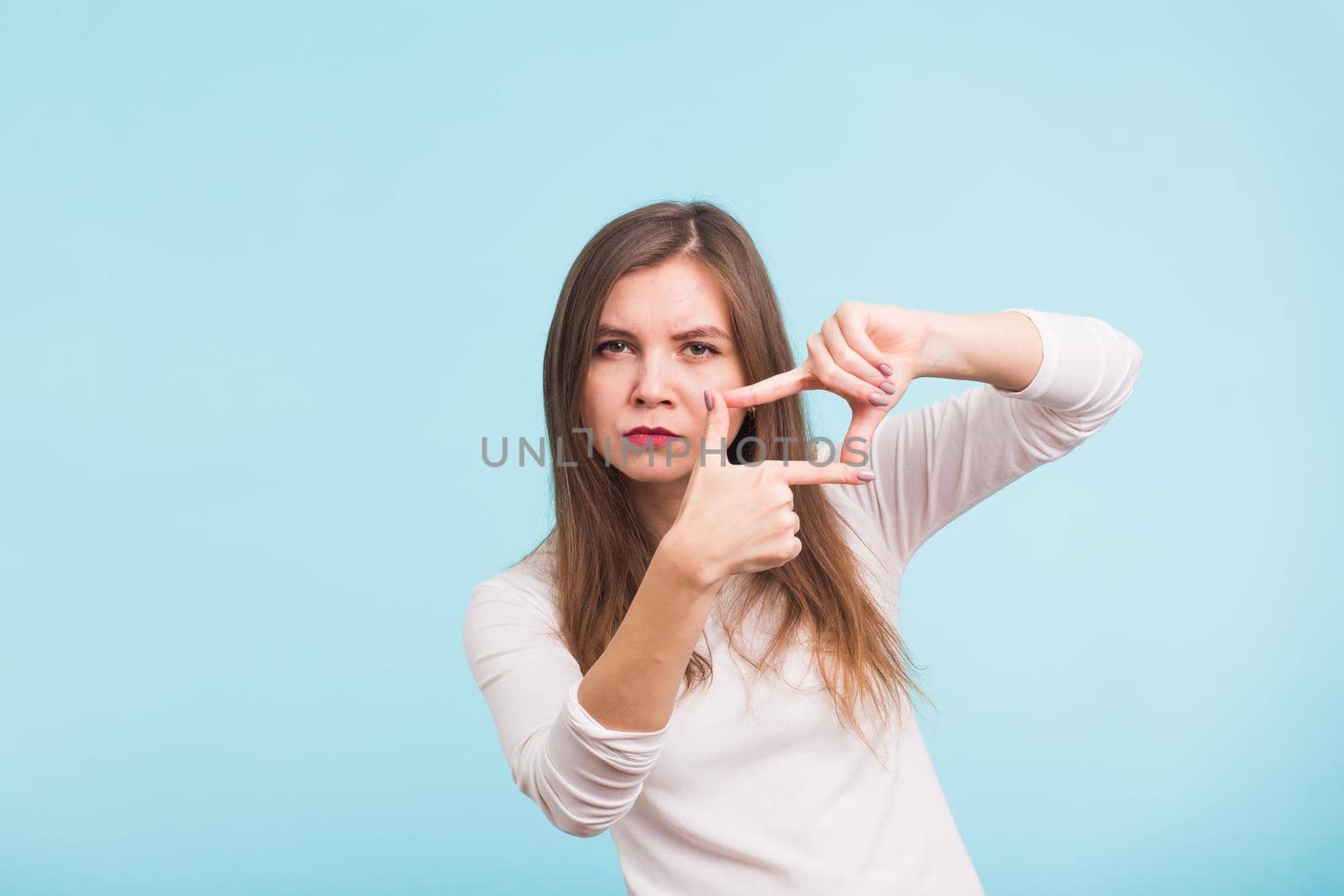 Young beautiful woman making a camera frame with fingers. Isolated on blue background