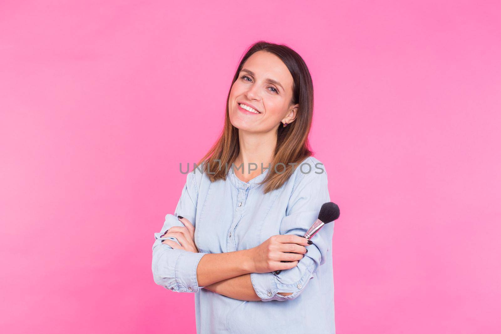 Professional makeup artist with brushes on pink background.