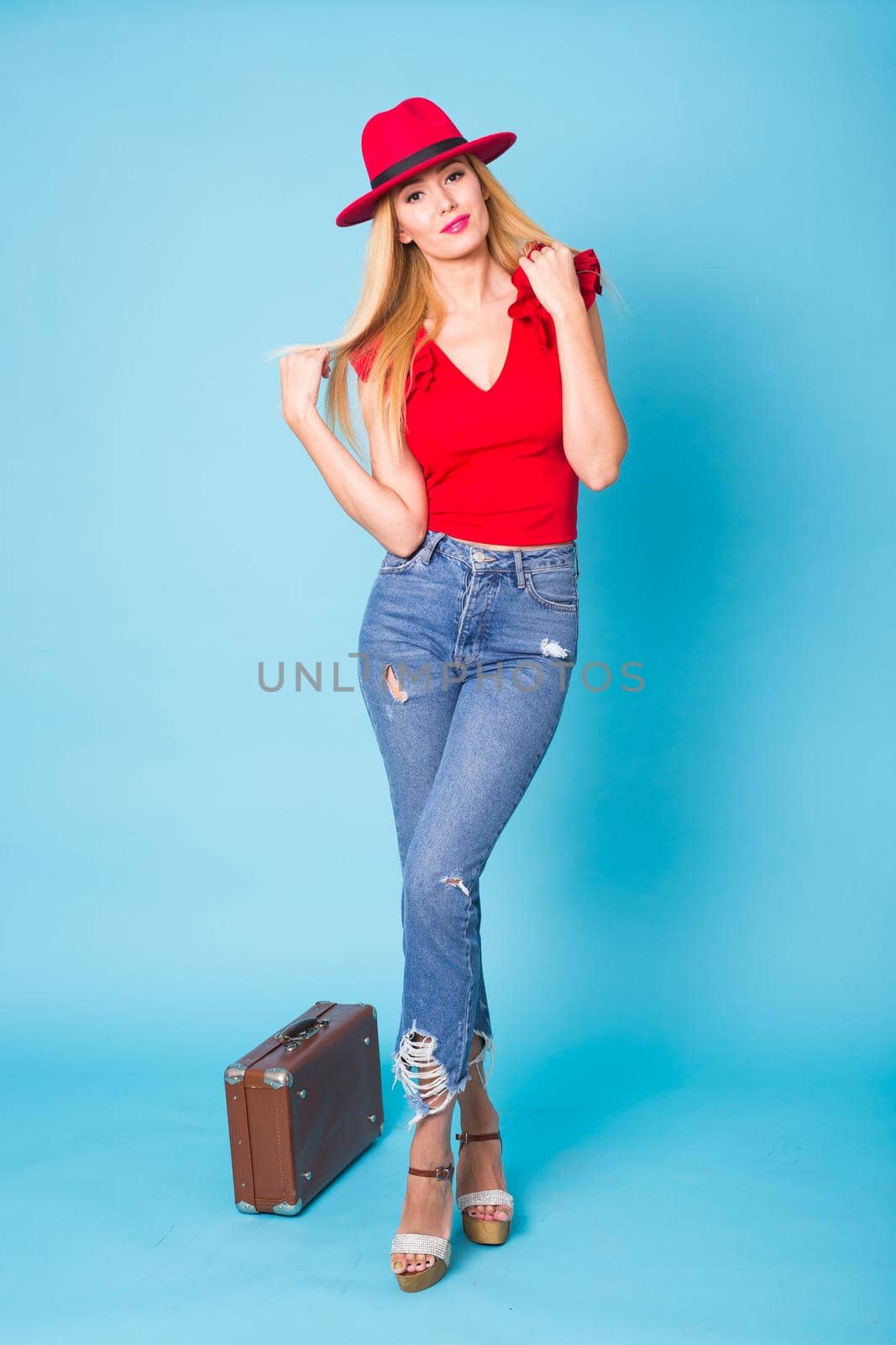 Summer, fashion and holiday concept - Beautiful blonde woman with retro suitcase on blue background.