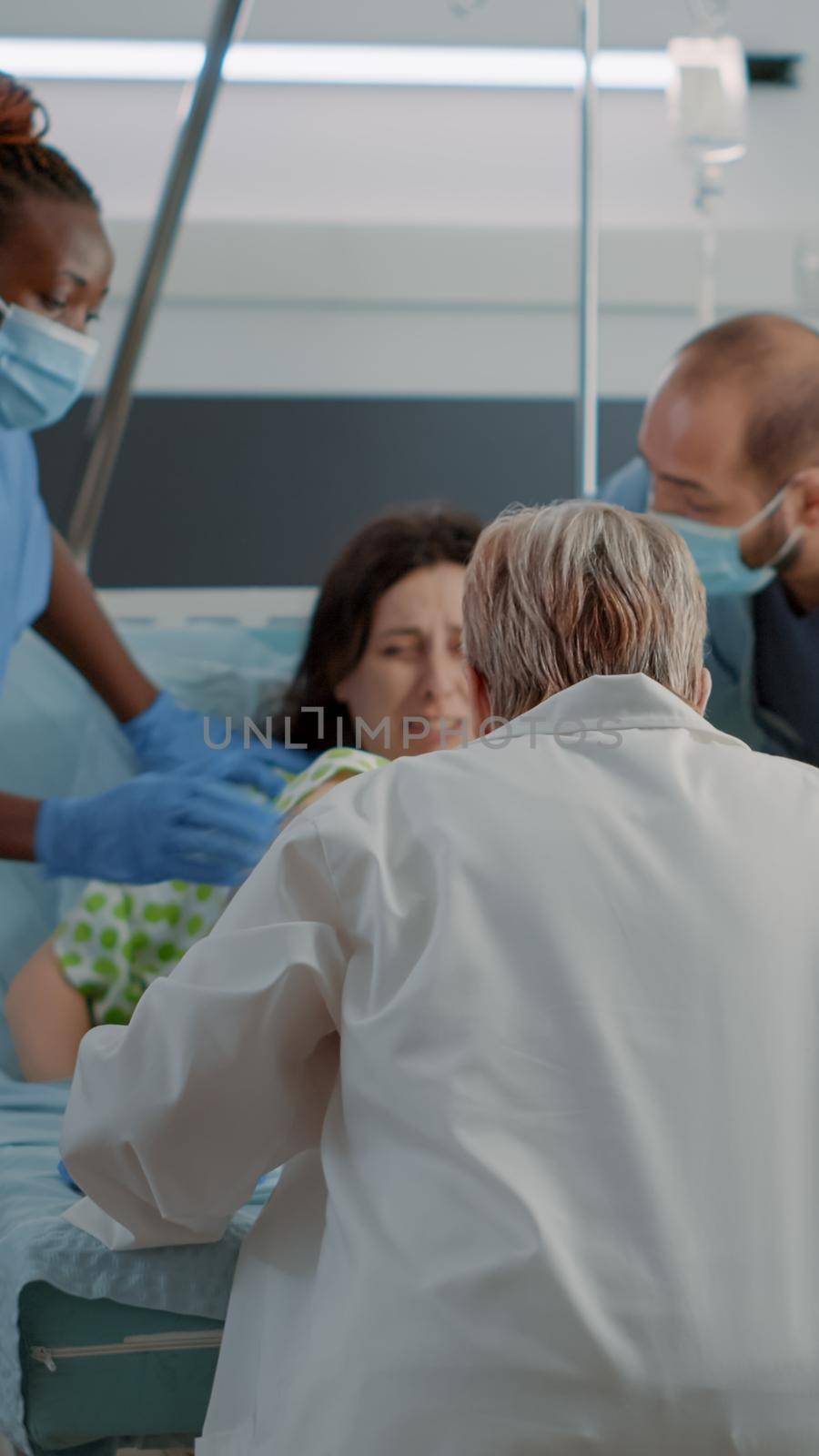 Obstetrics doctor and african american nurse delivering child in hospital ward at maternity. Caucasian pregnant woman with painful contractions pushing for childbirth with father of child