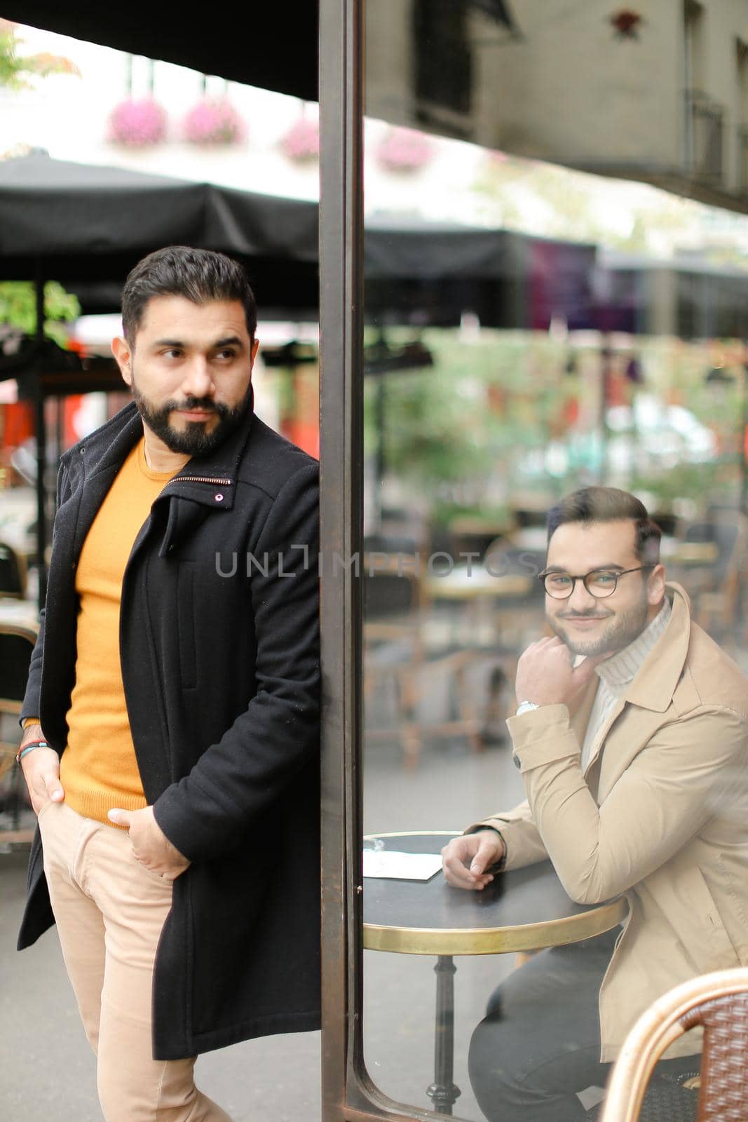 Young fashionable man standing at street cafe outside near sitting man. by sisterspro