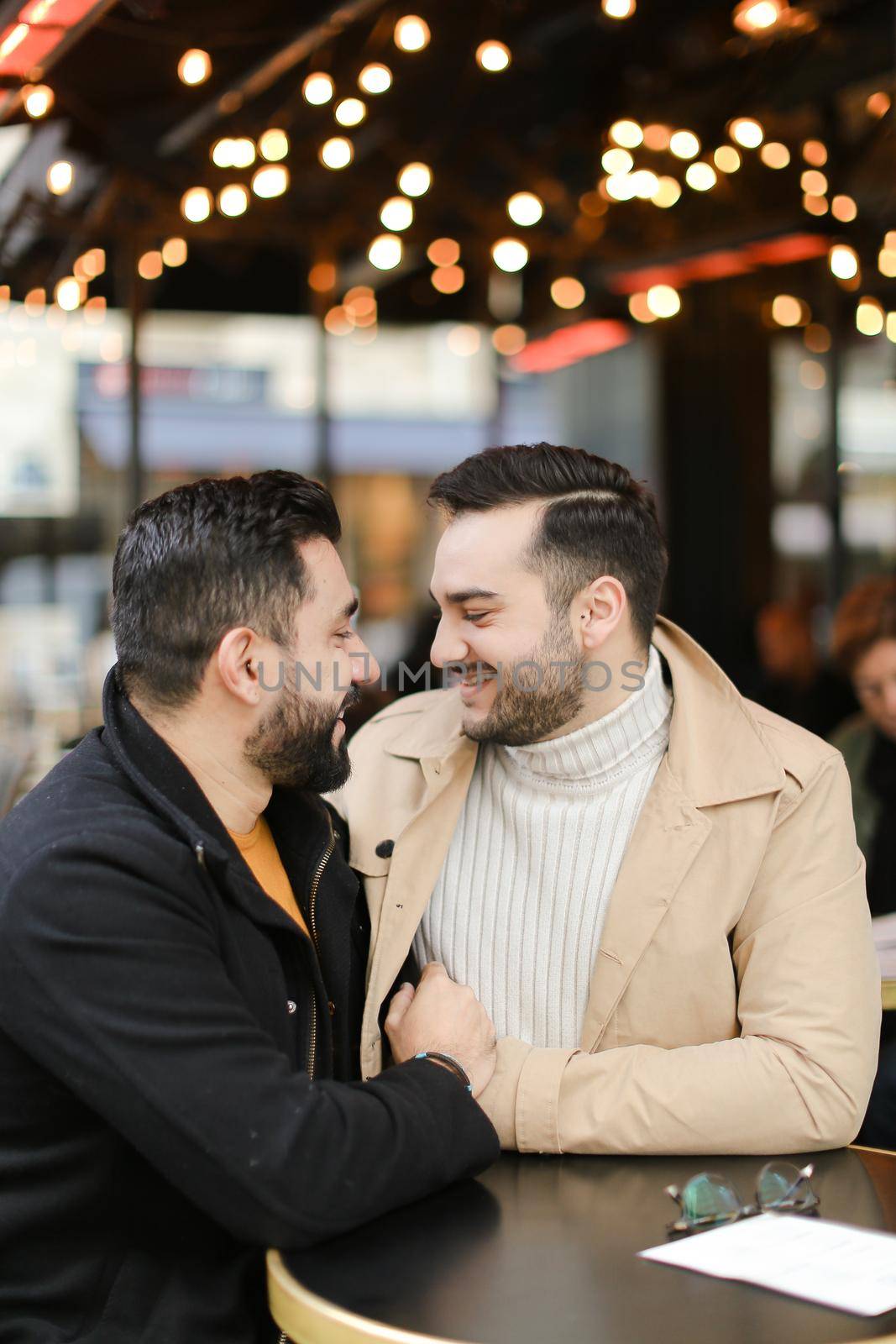 Caucasian gays sitting at street cafe, speaking and hugging. Concept of relationship and same sex couple.