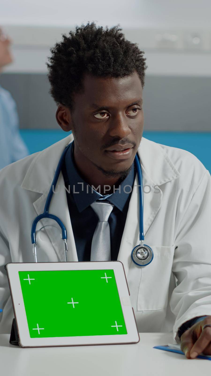 Man working as doctor pointing at green screen on modern tablet in office. Medic with horizontal mockup template and isolated chroma key technology for appointment at medical facility