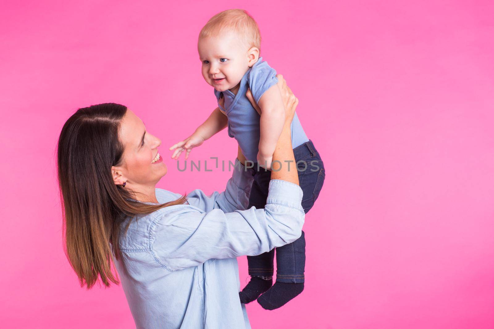 family, motherhood, parenting, people and child care concept - happy mother holds adorable baby over pink background.