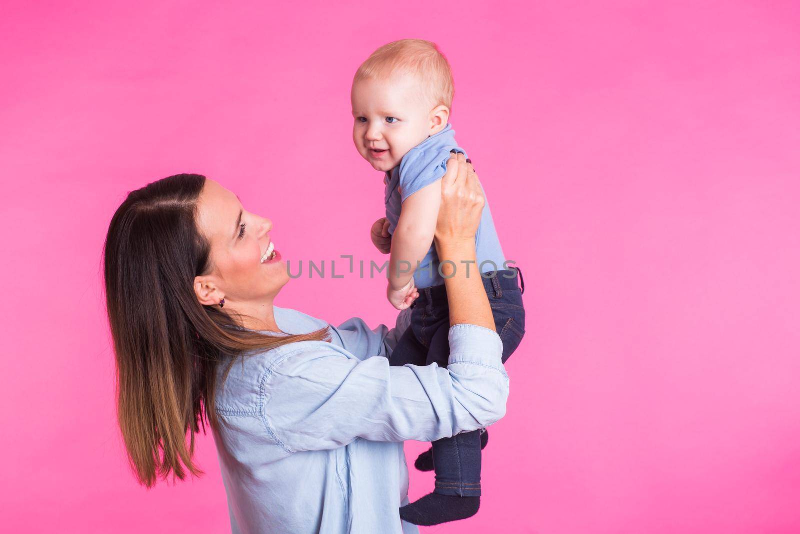 family, motherhood, parenting, people and child care concept - happy mother holds adorable baby over pink background.