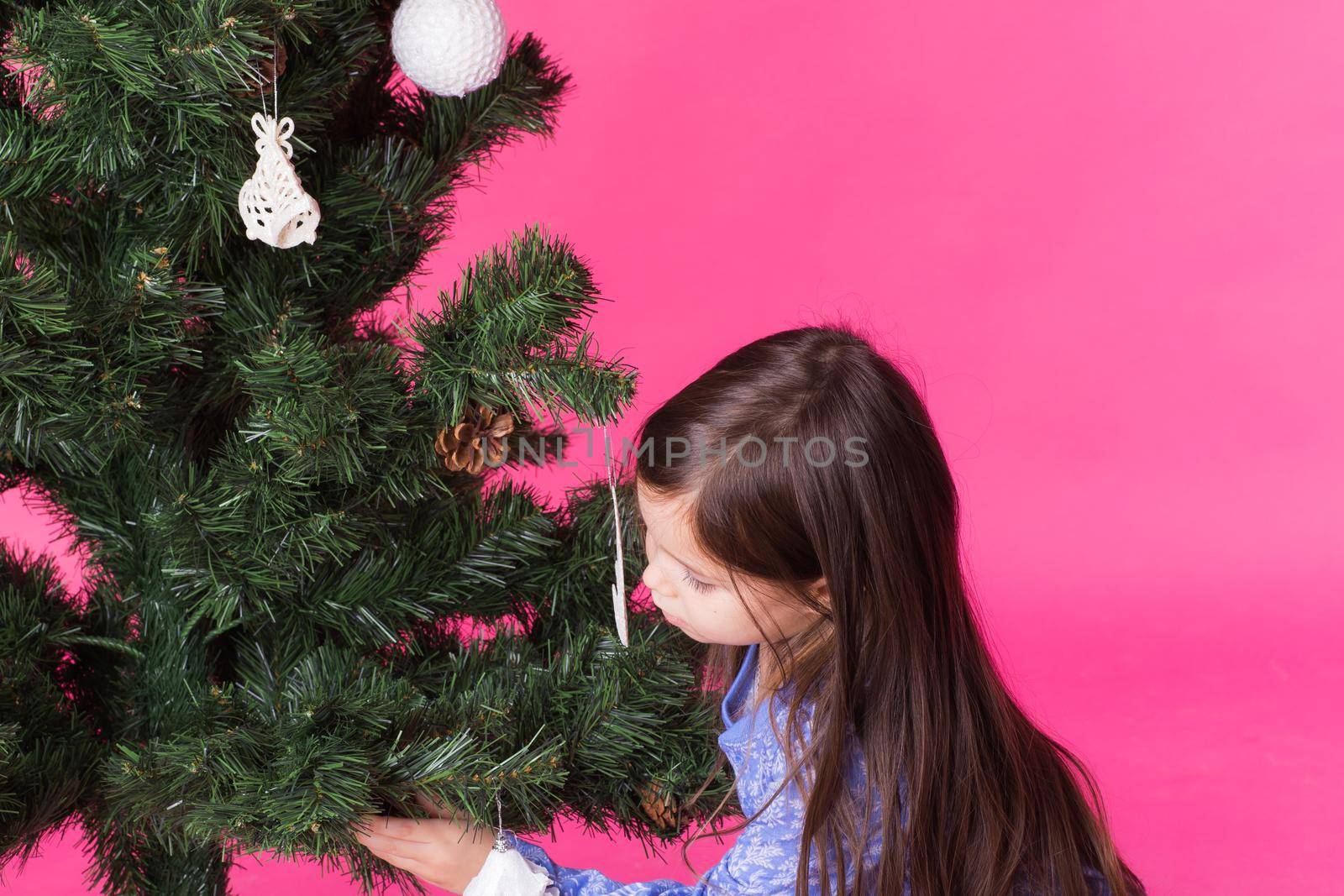 Children, holidays and christmas concept - little girl decorating christmas tree on pink background by Satura86