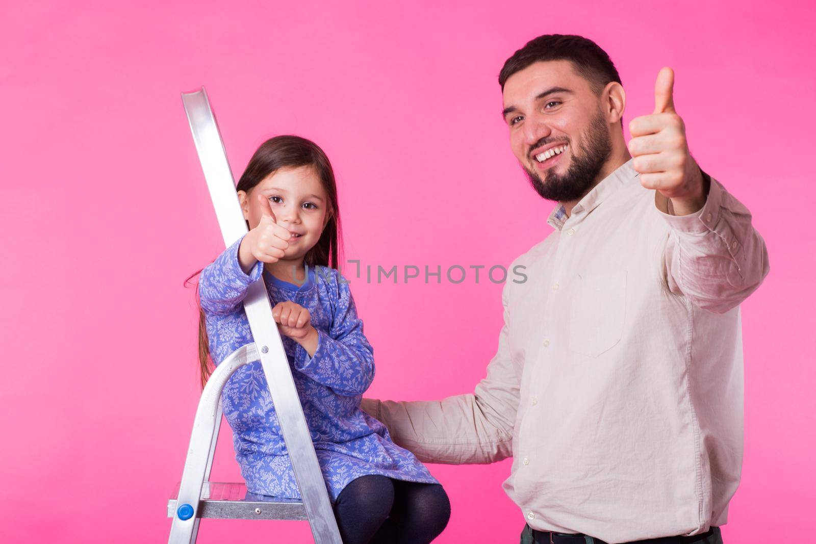 Father and her little daughter with thumbs up over pink background. Adult man and baby girl are happy.