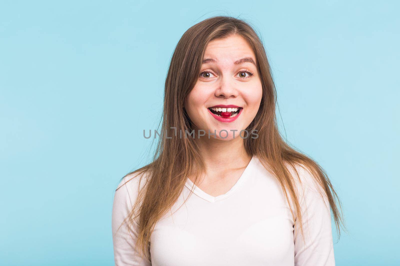 Red tablet in the mouth of the woman on blue background.