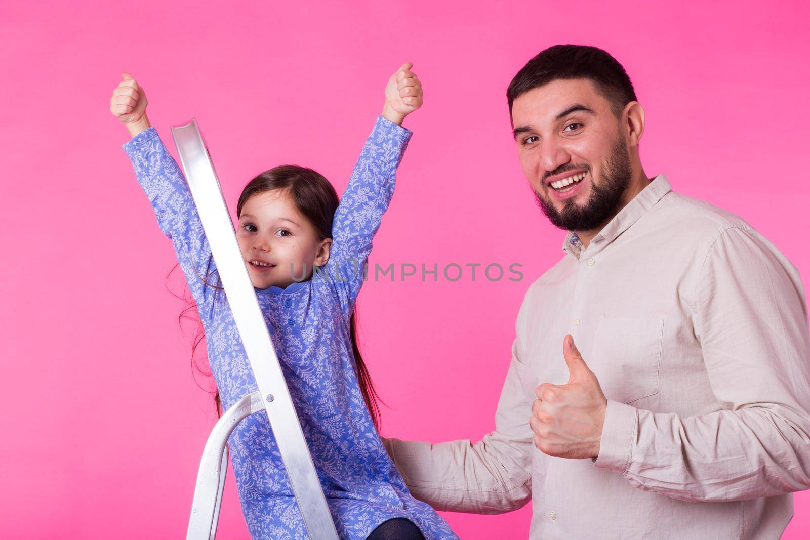 Father and her little daughter with thumbs up over pink background. Adult man and baby girl are happy.