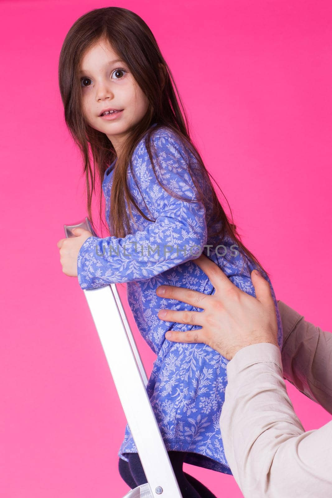 happy little girl on a folding ladder over pink background.