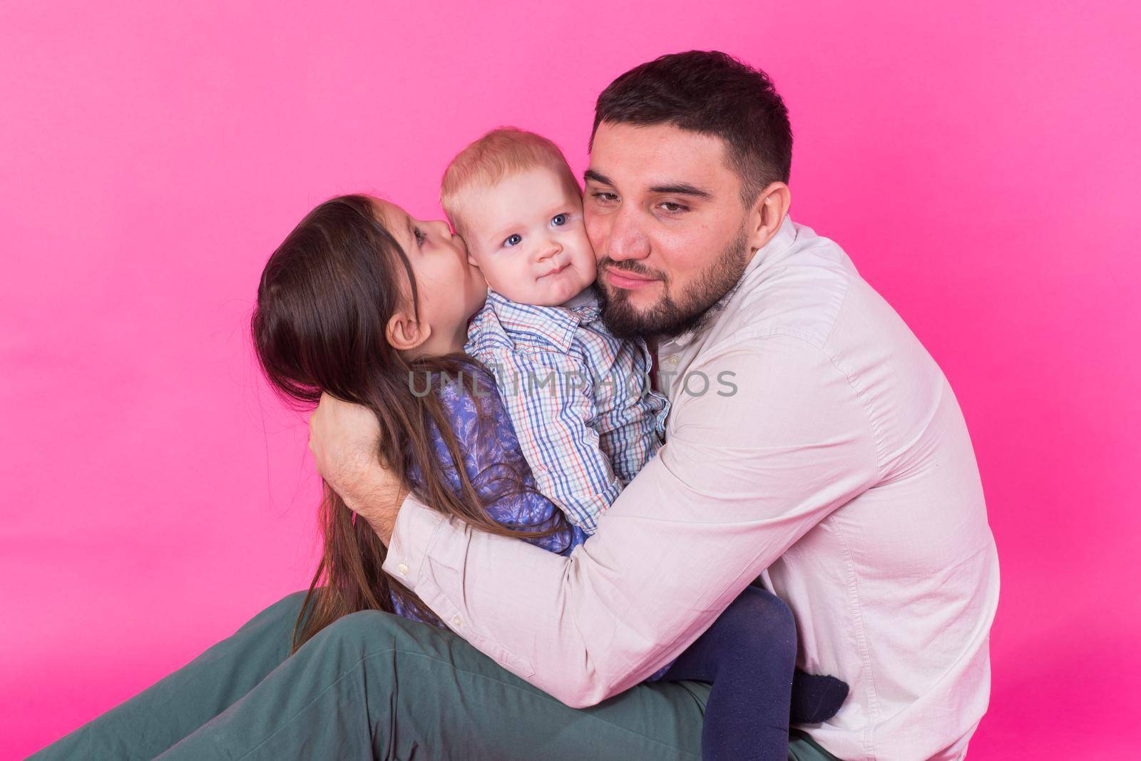 handsome father carrying his little daughter and baby son on pink background.