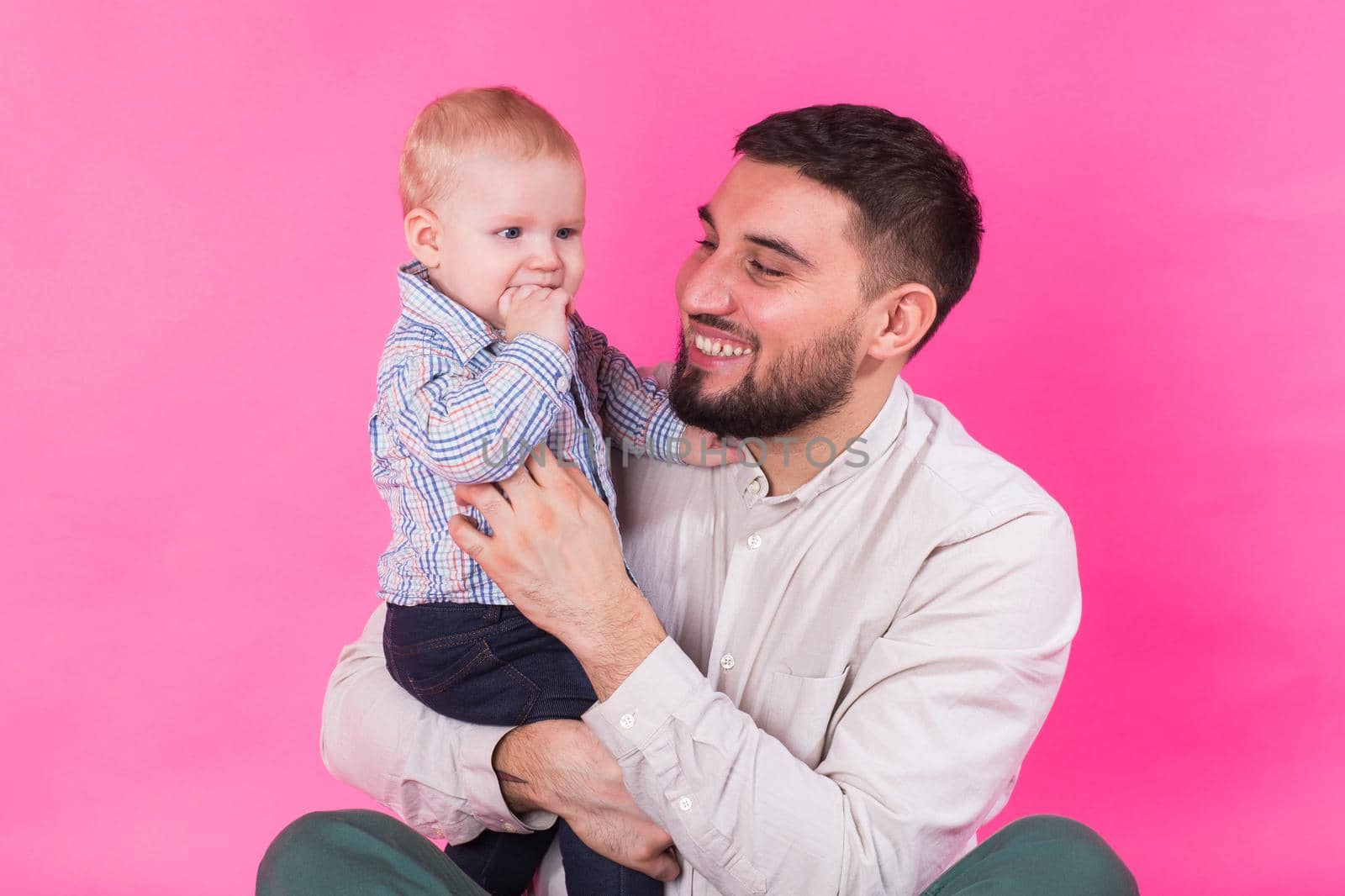 Happy portrait of the father and son on pink background. In studio.