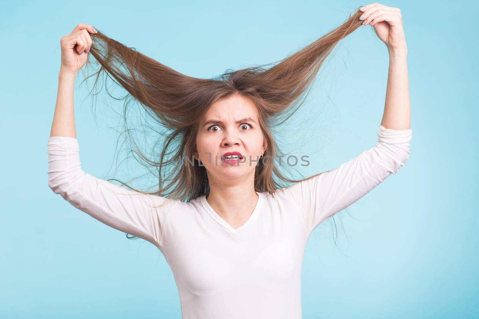 Young woman with unhealthy long hair keep hair in hand with nature make up portrait isolated on blue by Satura86