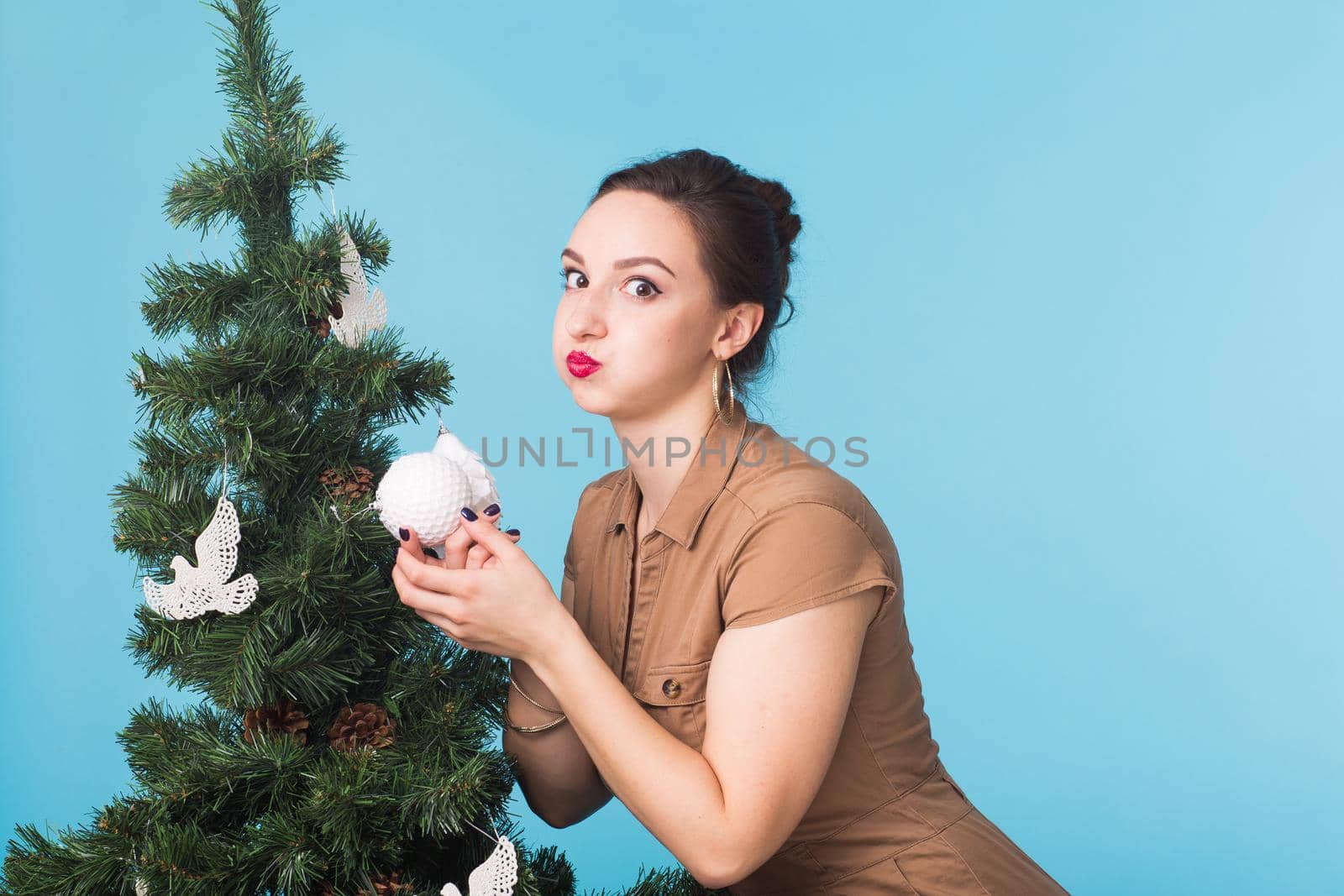 People and holidays concept - Portrait of smiling young woman with Christmas tree on blue background