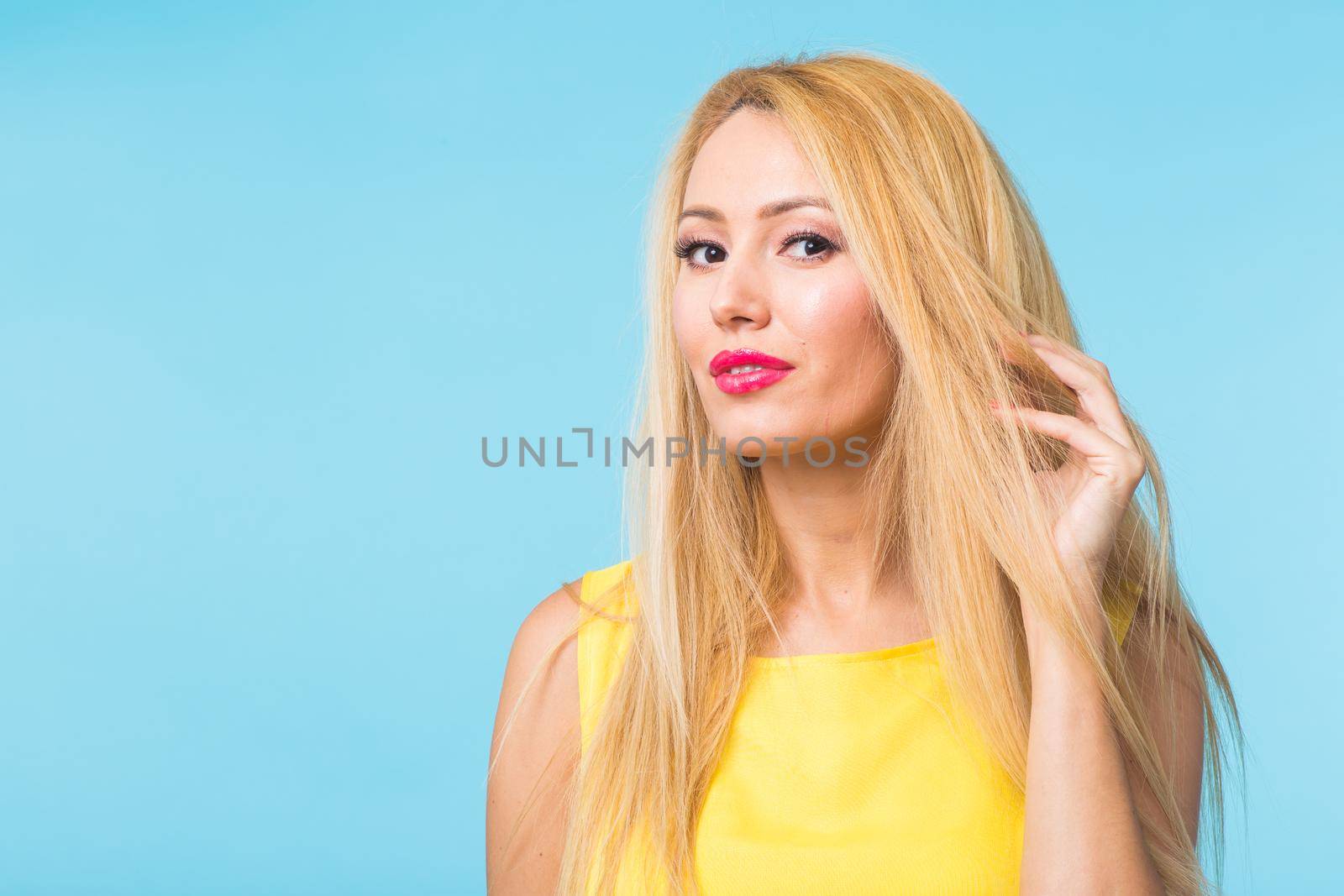 Beautiful woman with long straight blond hair. Fashion model posing at studio on blue background with copyspace by Satura86