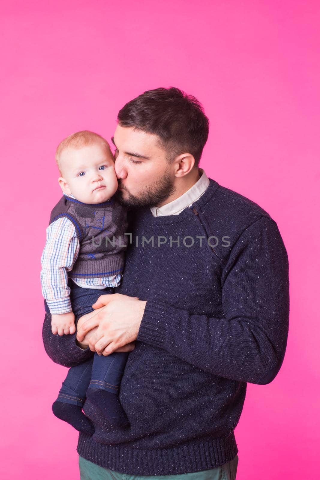 Happy father holding baby son in hands over pink background.