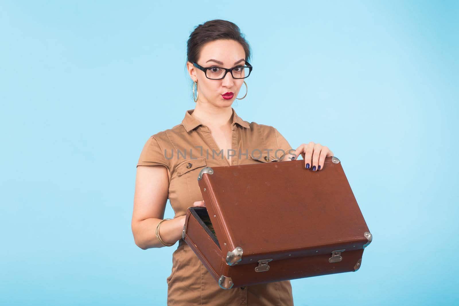 Portrait of excited young woman holding a suitcase isolated over blue background, Travel, holidays and vacation concept