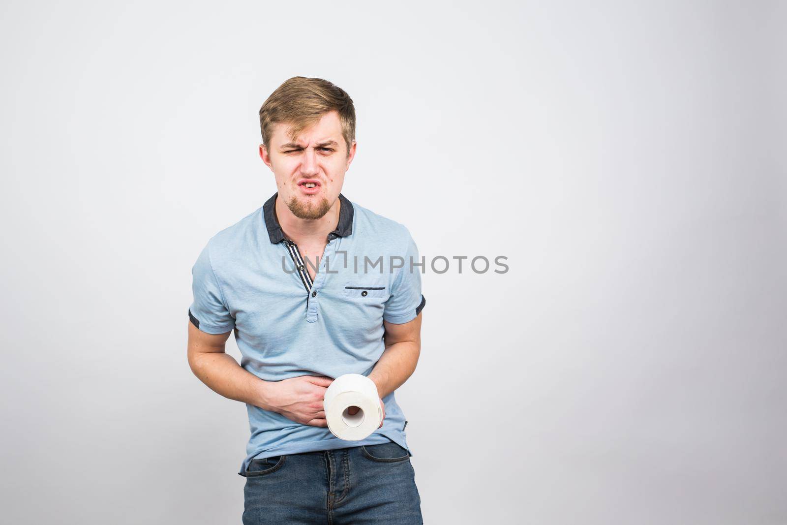 Man with stomach pain and toilet paper roll on white background.