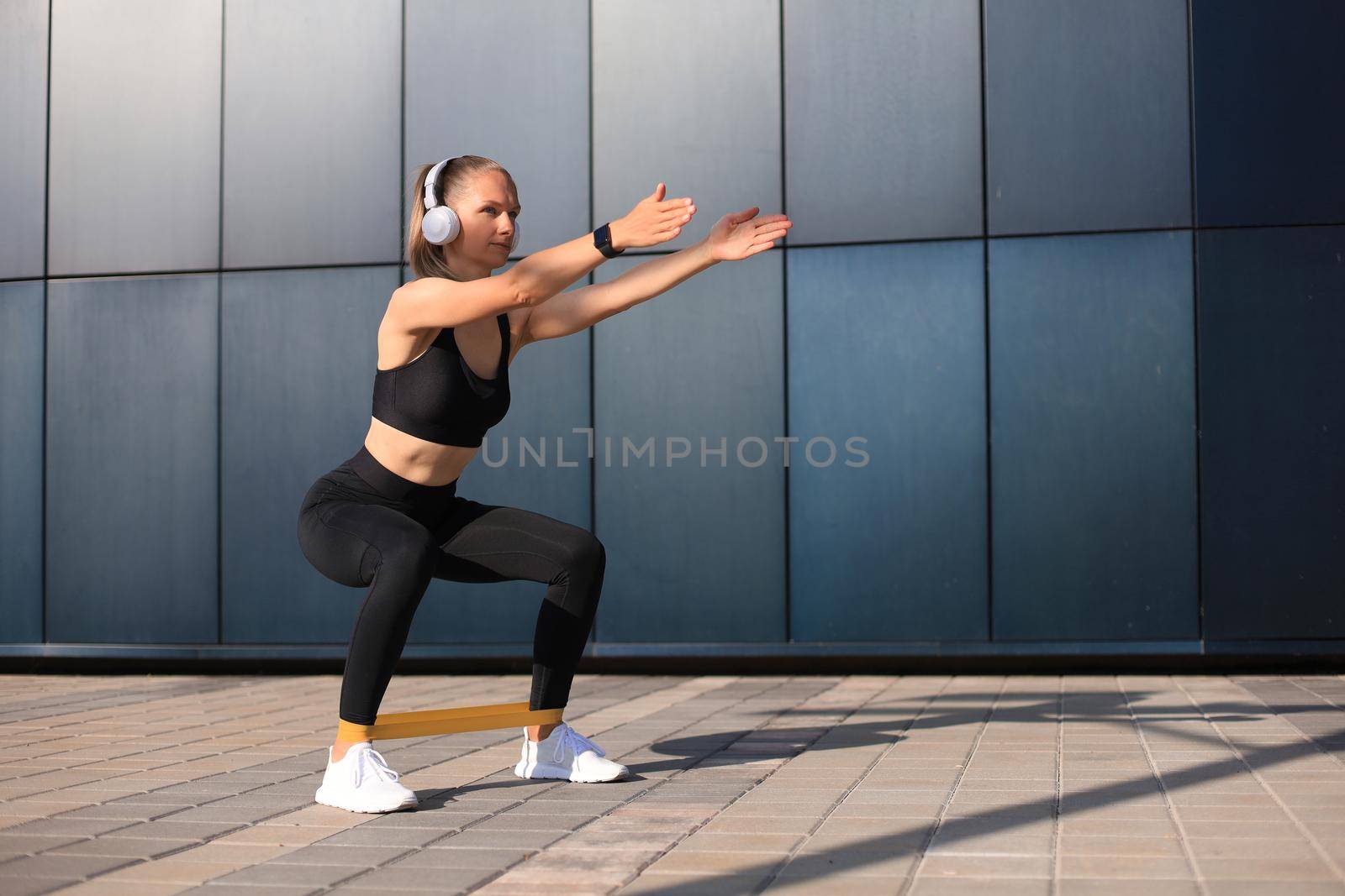 Sporty woman doing squats with fitness gum expander outdoors. by tsyhun